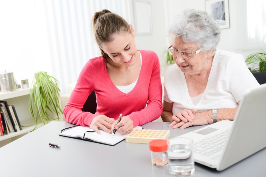 a young woman works with an elderly woman via computer and a notebook as part of mobile medication monitoring